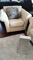 Cream leather armchair with curved arms on dark wood floor, beige carpet partially visible