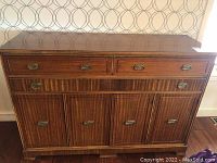 Front view of wood sideboard showing multiple drawers and cabinets with brass hardware