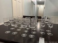 Full set of 12 wine glasses and 4 champagne glasses arranged on table, showing overall quantity and style, geometric grid pattern visible on all glass bowls.