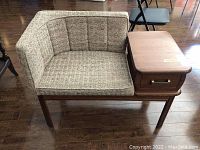 Front and side view of the vintage phone table bench showing wood frame, upholstered seat and back, and faux drawer with brass handle.