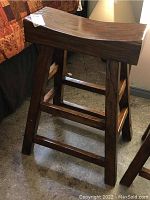 Side angle of handcrafted hardwood stool showing contoured seat, sturdy legs, and robust construction