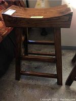 Front angled view of handcrafted wooden stool showing curved top and sturdy legs