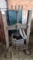 Full view of antique wooden grape wine press featuring the vertical wormwood screw and wooden slat basket showing some damage.