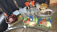 Full kitchenware lot on glass tabletop showing bowls, glasses, plates, silver tray and decorative golden bowl