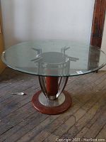 Full view of the large round table showing the glass top and the wood and metal base on a wooden floor.