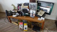 Wide view showing miscellaneous electronics arranged on a wooden table including headphones, phones, chargers, and a small space heater.