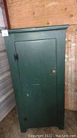 Closed view of the deep green painted pine cabinet with single door and black hinges.