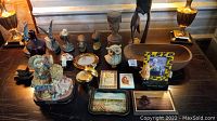 Various trinkets including carved wooden figurines, ceramic pieces, framed photos, and decorative items arranged on a wooden surface.