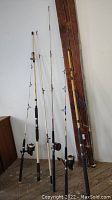 Full view of six fishing poles of varying lengths and styles showing bamboo and fiberglass materials, with some reels attached.