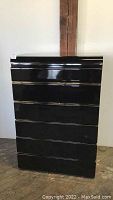 Full front view of tall black dresser with shiny finish and brass details in situ.