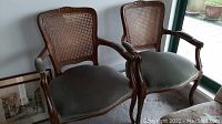 Front view of two wooden accent armchairs with cane backs and fabric seats showing overall condition and style.