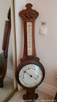 Full view of the tall wooden carved barometer with round dial and integrated thermometer.