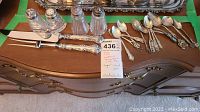 Full lot showing carving knives, teaspoons, salt and pepper shakers, and part of a serving tray on a wooden dresser surface with green tape markings