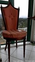Full view of a tufted fabric chair with wood legs and carved trim, peach/pink upholstery, high back, visible stains on seat and backrest.