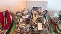 Full view of the complete silver plate coffee and tea service including tray, coffee pot, tea pot, creamer, sugar bowl, forks and spoons.