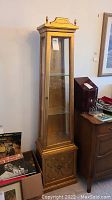 Full view of the tall gold tone display cabinet with glass panels and a bottom storage compartment.