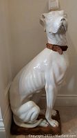Full view of seated white ceramic dog statue on base