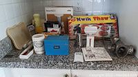 Overview of all kitchen items spread on countertop showing Braun meat grinder box, Kwik Thaw product box, food scale, thermometers, aprons, and recipe box.
