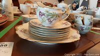 Photo showing cups stacked inside the matching saucers and stacked side plates with creamer on top, all with floral and gold trim design.