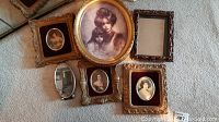 Six metal picture frames of various sizes and shapes laid out on carpet, showing different portraits and empty frame.