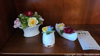 Three hand-painted porcelain flower arrangements displayed together on a wooden shelf.