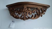 Front view of ornate decorative wall shelf with intricate scrollwork in gold/bronze finish