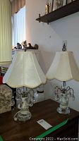 Pair of matching pale blue porcelain table lamps each with hanging crystal jewels and cream-colored scalloped lampshades on wooden surface near window and sofa