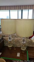 Pair of matching table lamps shown side by side on wood surface in front of window, showing overall height and shades