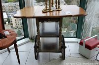 View of entire wooden teacart showing expanded tabletop with leaves and items on top. Shows medium wood stain and turned legs.