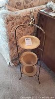Side view of the three-tiered stand showing brass frame and cream plastic plates with wear.