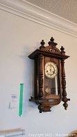 Full view of wooden wall clock mounted on wall showing entire clock structure.