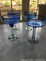 Four margarita glasses with blue rims displayed on a table, viewed from the side with natural light.