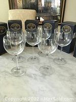 Six clear wine glasses displayed standing on a flat surface in front of their individual black and gold branded boxes.