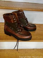 Side angle view of the brown and olive leather boots on wooden stairs showing front and side details.