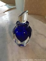 Blue cobalt art crystal perfume bottle with thick clear glass accents and clear stopper on marble surface.