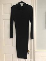 Front view of elegant black dress hanging on a door, showing draped high neckline, long sleeves, and slim fit.