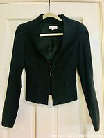 Front view of black fitted Emporio Armani women's jacket on hanger against white door background.