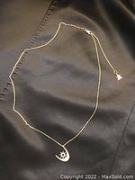 The full necklace laid on a black fabric background showing the gold chain and crescent moon pendant with diamond detailing.