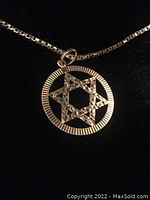 Close-up photo of the textured gold Star of David pendant with circular frame on the necklace chain.