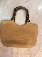 Front view of handbag showing woven texture and beaded handle detail.