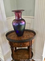 Photo of the iridescent art glass vase placed on a decorative wooden table, showing its full shape and vivid color reflections.