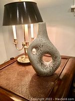 Front view of the Jonathan Adler pottery sculpture on a table near a lamp showing the textured surface and cut-out holes.