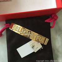Gold tone bracelet with rhinestones spelling 'DELIGHTFUL' displayed on black pouch with red drawstring and white tag visible