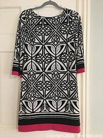 Front view of women's dress with black and white geometric print and pink trim on sleeves and hem.