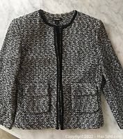 Front view of the black and white tweed jacket showing the pattern, black trim detail, and front patch pockets.