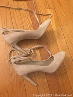 Side and top angle showing one beige suede BCBG high heel shoe with ankle wrap tie and pointed toe on wood flooring.