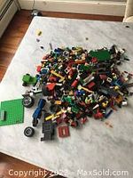 Photo showing a large pile of assorted LEGO pieces including bricks, wheels, mini-figures, and base plates on a white surface.