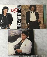 Front covers of Michael Jackson Bad, Off The Wall, and Thriller albums laid out on a marble surface
