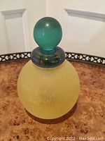 Murano art glass bottle standing upright showing the yellow textured body, blue rim, and green stopper.