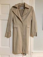 Front view of beige Nine West ladies coat hanging on door showing full length and design details.